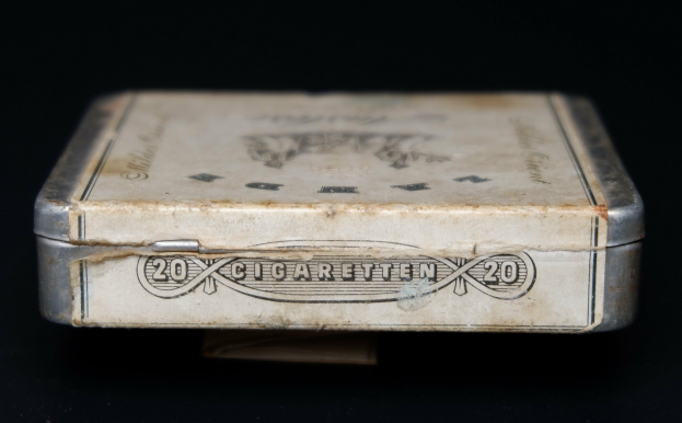 Alte Metall-Zigaretten-Dose mit Text auf einem schwarzen Tisch, die einen vintage-Eindruck vermittelt.