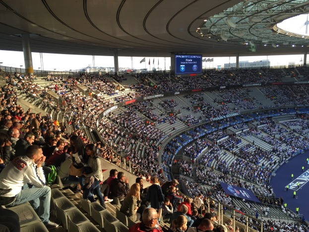 Große Menschenmenge in einem Stadion bei einem Fußballspiel, mit einer Bühne und Fahnen im Hintergrund.