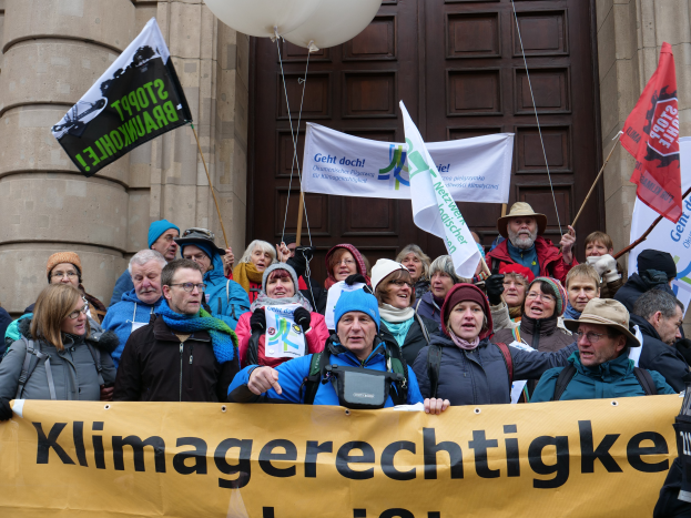 Eine Gruppe von Menschen vor einem Säulengebäude mit einer Tür, die eine Transparente mit Text, Fahnenstangen und Luftballons halten, nimmt an einem Klimastreik in Deutschland teil.