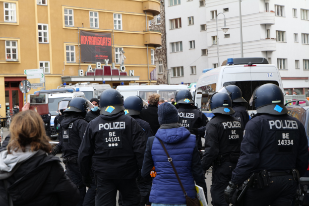 Polizeibeamte in Uniform vor einer Menge von Menschen, einige mit Helmen und Jacken, während einer Demonstration in Berlin, Deutschland.