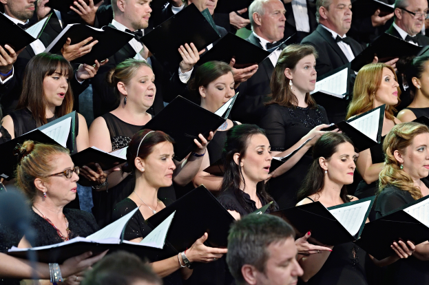 Eine Gruppe von Menschen steht vor einem Chor und hält jeweils ein Buch in der Hand, scheinbar im Einklang singend.