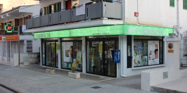 Apotheke an einer Straßenecke mit Gebäuden, Fahrzeugen und einem klaren blauen Himmel im Hintergrund.