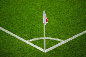 Ein Fußballfeld mit grünem Rasen, weißen Begrenzungslinien und einem weißen Pfosten mit einer roten und weißen Flagge in der Mitte des Strafraums.