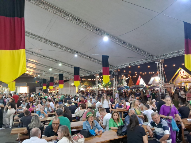 Eine große Gruppe von Menschen sitzt an Tischen unter einem Zelt auf dem Oktoberfest in München, Deutschland, mit Taschen und Gegenständen auf den Tischen und festlicher Décoration im Hintergrund.