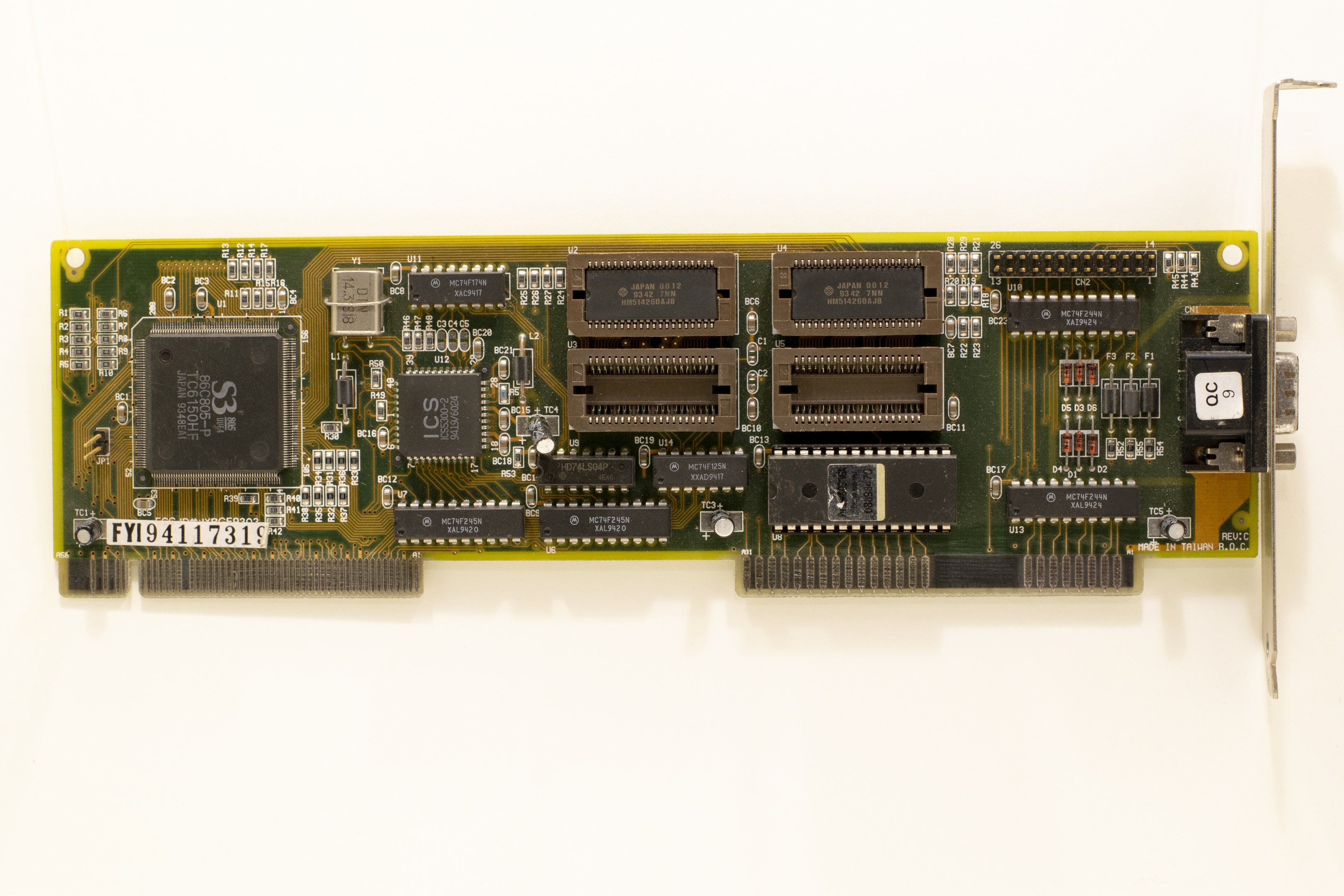 Nahaufnahme einer PCI-E-Karte mit einem zentralen Chip und mehreren Verbindern auf einer weißen Oberfläche.