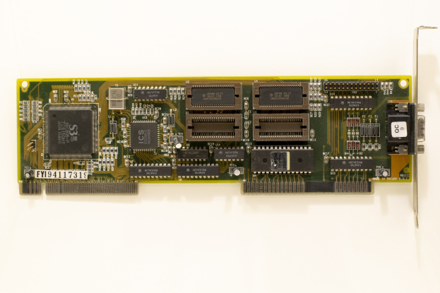 Nahaufnahme einer PCI-E-Karte mit einem zentralen Chip und mehreren Verbindern auf einer weißen Oberfläche.