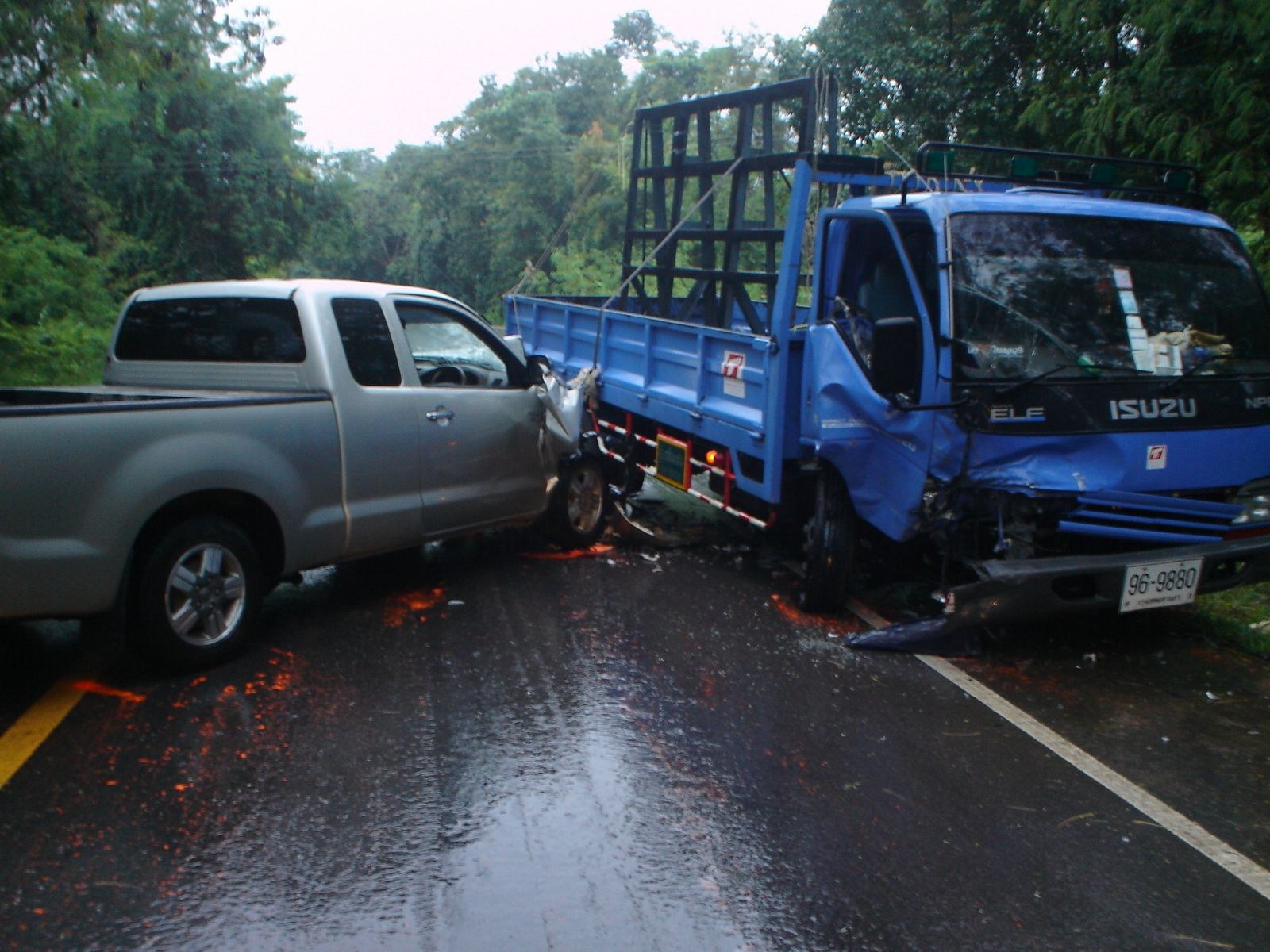 Ein schwerbeschädigter Truck mit eingedrückter Front und verbeulter Karosserie liegt am Straßenrand, umgeben von Bäumen unter einem klaren blauen Himmel.