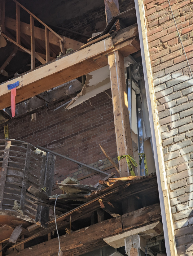 Ein teilweise abgerissener Bau mit verstreuten Holzplanken und Trümmern, zerbrochene Fenster und Türen.