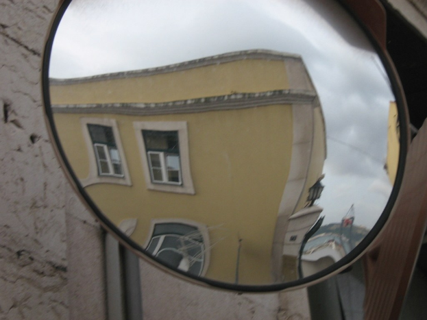 Reflexionen von Gebäuden, Licht und Himmel auf einem Straßenverkehrsspiegel mit einer Wand im Hintergrund.