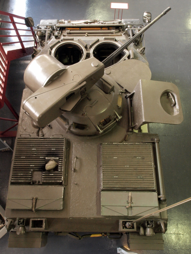 Ein großer Militärpanzer mit sichtbaren Ketten und Turm steht auf einem Boden, mit einem Metallgeländer auf der linken Seite.