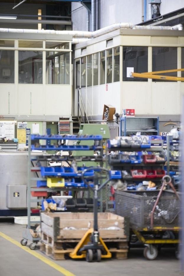 Großer Lagerraum mit verschiedenen Geräten, einschließlich fahrbaren Wagen, Schränken und einer Kiste, mit einer Glasfensterwand und Rohren im Hintergrund.