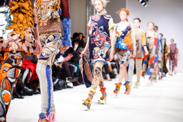 Eine Gruppe Von Frauen, Die Eine Laufsteg In London Fashion Week Heruntergehen, Mit Einem Publikum Im Hintergrund Unter Helllem Licht.
