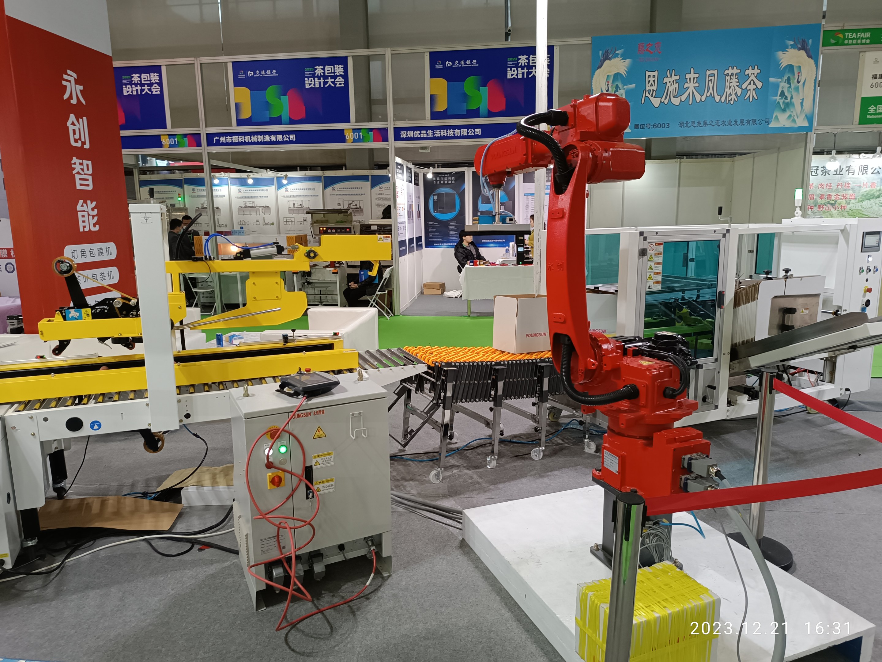 Gruppe von Robotern auf einem Tisch in einer Fabrikumgebung umgeben von Maschinen, Kabeln, Leiterplatten und beleuchteten Komponenten, mit Menschen im Hintergrund.