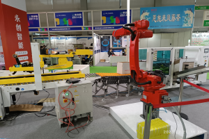 Gruppe von Robotern auf einem Tisch in einer Fabrikumgebung umgeben von Maschinen, Kabeln, Leiterplatten und beleuchteten Komponenten, mit Menschen im Hintergrund.