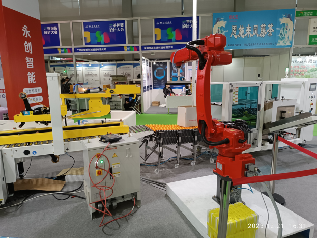 Gruppe von Robotern auf einem Tisch in einer Fabrikumgebung umgeben von Maschinen, Kabeln, Leiterplatten und beleuchteten Komponenten, mit Menschen im Hintergrund.