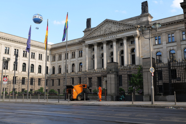 Großer moderner Bau mit vielen Fenstern, als Bundestag in Berlin identifiziert, umgeben von Straßeninfrastruktur und Passanten unter einem bewölktem Himmel.
