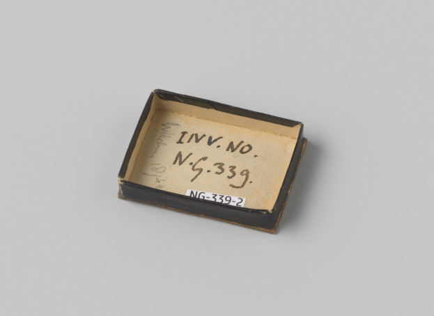 Kleiner schwarzer Kasten mit einem weißen Etikett auf einer weißen Oberfläche, Etikett hat Text.