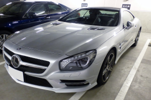 Silberner Mercedes-Benz SL-Class in einer Mehrgeschossigen Parkgarage neben anderen Fahrzeugen geparkt, mit Texttafeln an den Wänden sichtbar.