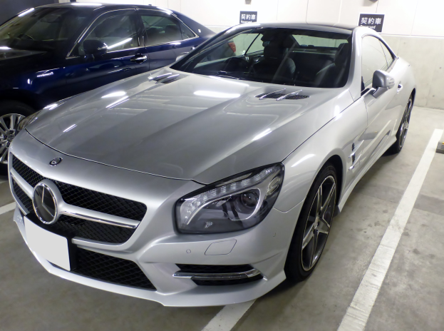 Silberner Mercedes-Benz SL-Class in einer Mehrgeschossigen Parkgarage neben anderen Fahrzeugen geparkt, mit Texttafeln an den Wänden sichtbar.