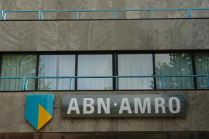 Ein Gebäude mit einer Tafel, auf der 'ABN AMRO' steht, mit einem Brett, auf dem Text steht, Geländern und Glasfenstern mit Vorhängen, mit Text unten, der eine Strafe von 1,5 Milliarden Dollar durch die Europäische Union erwähnt.