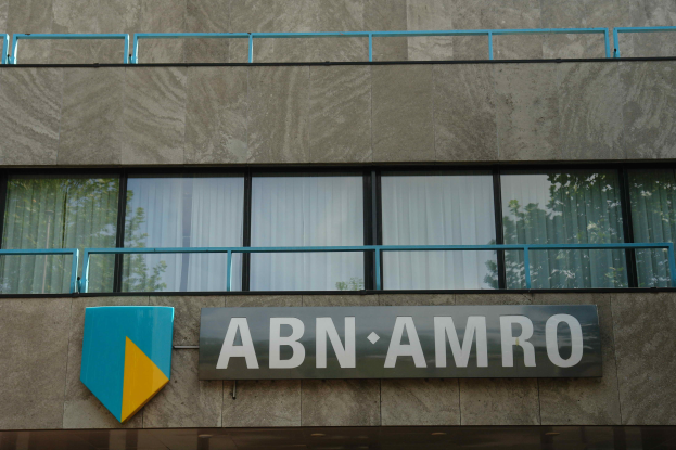 Ein Gebäude mit einer Tafel, auf der 'ABN AMRO' steht, mit einem Brett, auf dem Text steht, Geländern und Glasfenstern mit Vorhängen, mit Text unten, der eine Strafe von 1,5 Milliarden Dollar durch die Europäische Union erwähnt.