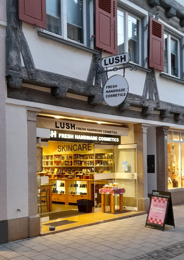Verkaufsfläche von Lush Skincare mit Innenausstattung, einschließlich Schränken, einem Schreibtisch und einem Stuhl, die durch das Fenster zu sehen sind.
