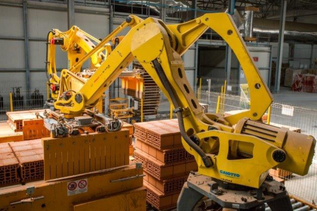 Großes Industriegelände mit gestapelten Kisten, Kränen, Zaun, Strommasten und einer fernen Mauer.