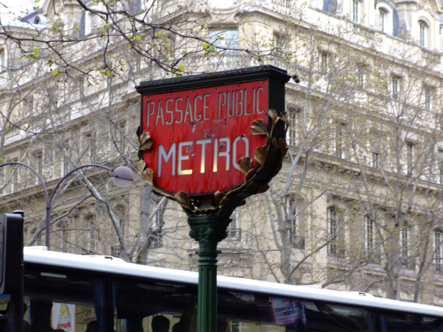 Rote Tafel an einem Pfahl in der Nähe, ein Bus an einer öffentlichen U-Bahn-Station in der Mitte und ein Gebäude mit Fenstern, Bäumen und einem klaren blauen Himmel im Hintergrund.