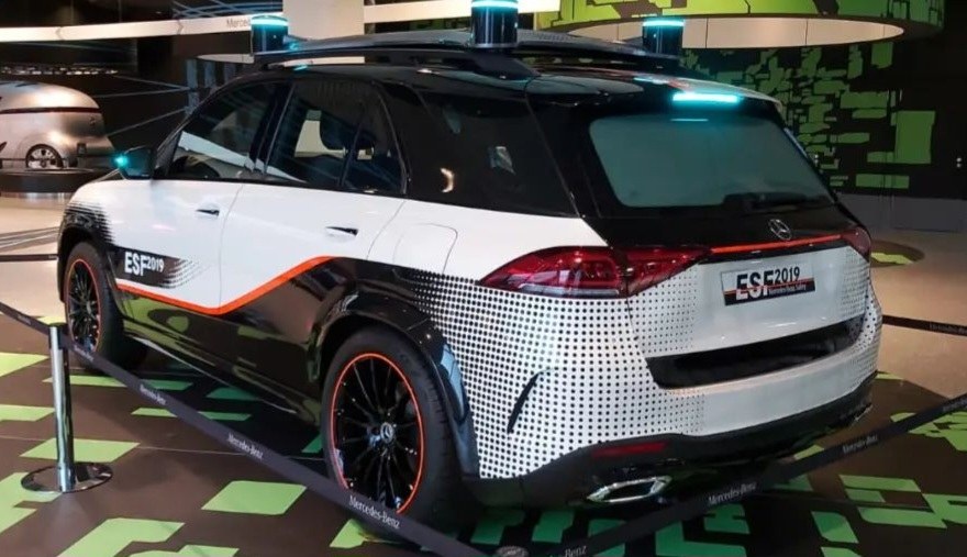 Mercedes-Benz E-Klasse Electric SUV auf der IAA in Frankfurt gezeigt, umgeben von Absperrpollern mit Seilen und Lichtern, mit einem weiteren Fahrzeug und Text an einer Wand im Hintergrund.