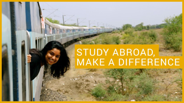 Frau in schwarzem Kleid, die lächelt, während sie an einem Zug lehnt, mit "Study Abroad, Make a Difference" darauf, vor einem Hintergrund aus Bäumen, Pfählen und einem klaren blauen Himmel.