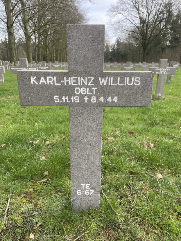 Grab von Karl-Heinz Willis auf einem deutschen Friedhof, umgeben von Gras und welken Bl├Ąttern mit Trees und einem klaren blauen Himmel im Hintergrund.