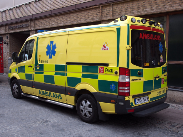 Ambulanz vor einem Backsteingebäude mit einem Feuerlöscher auf der linken Seite geparkt, auf der Straße, mit lesbarem Text auf dem Gebäude im Hintergrund.