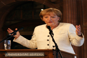 Bundeskanzlerin Angela Merkel hält eine Rede an der Universität Leipzig und steht an einem Rednerpult mit einem Mikrofon und einem Glas Wasser.