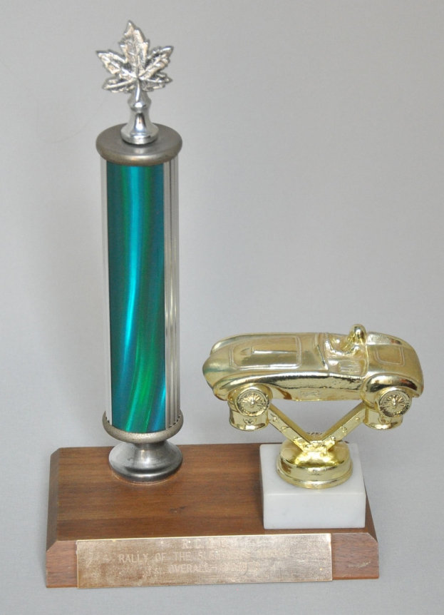 Ein glänzender, detaillierter Pokal mit einem Miniaturauto darauf, auf einer hellen Holzplatte montiert.