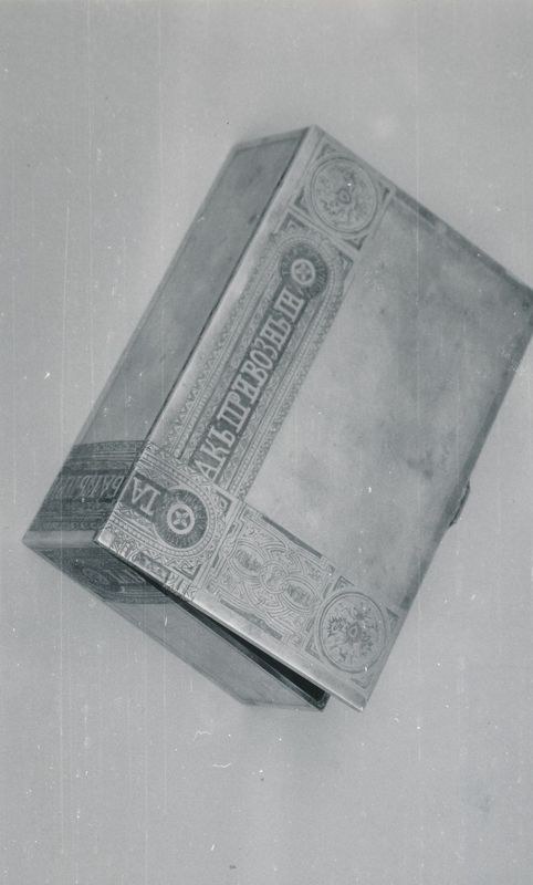 Schwarzes und weißes Foto einer rechteckigen Zigarettenbox mit offenem Deckel, der ein paar Zigaretten im Inneren enthüllt, auf einer weißen Oberfläche.