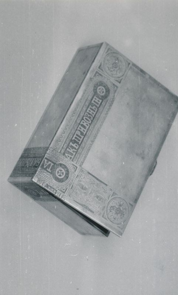 Schwarzes und weißes Foto einer rechteckigen Zigarettenbox mit offenem Deckel, der ein paar Zigaretten im Inneren enthüllt, auf einer weißen Oberfläche.