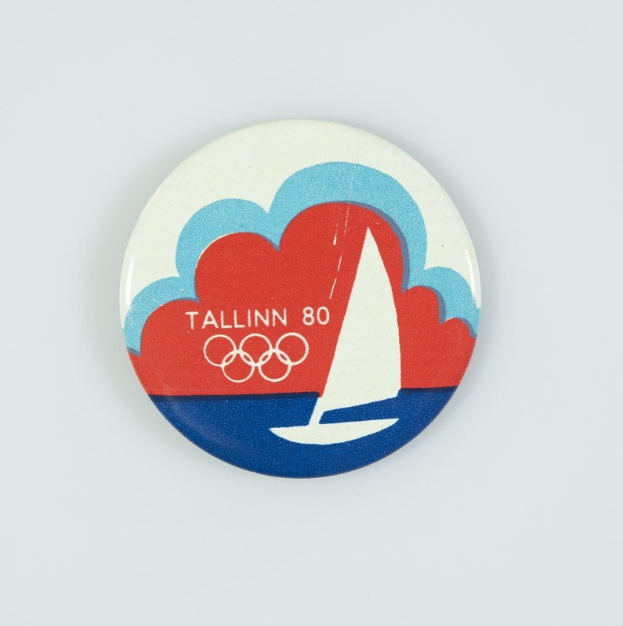 Ein weißes Abzeichen mit einem Segelboot-Design und der Aufschrift "Tallinn 80 Olympische Spiele", das den 80. Jahrestag der Olympischen Spiele in Tallinn feiert.