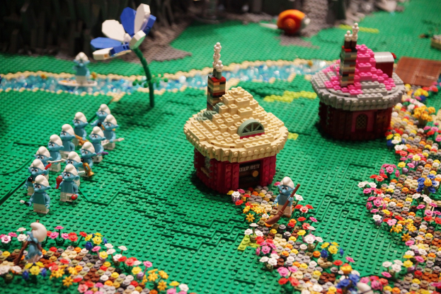 Ein Lego-Modell einer Kleinstadt mit bunten Blumen, Spielzeugen, Häusern, Pflanzen und anderen Gegenständen vor einem leicht unscharfen, träumerischen Hintergrund.