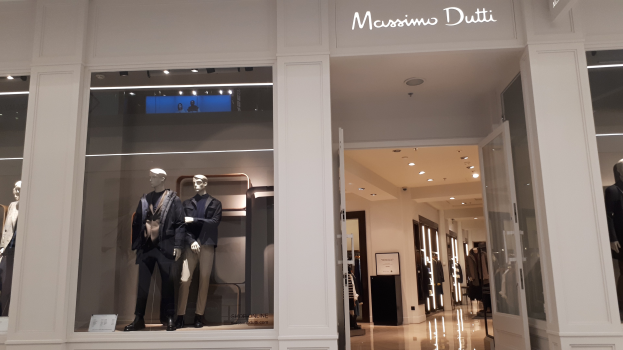 Vitrine des Massimo Dutti in Mailand, Italien mit Schaufensterpuppen in zeitgenössischer Mode, Innenbeleuchtung, Informationsschildern und Türen.