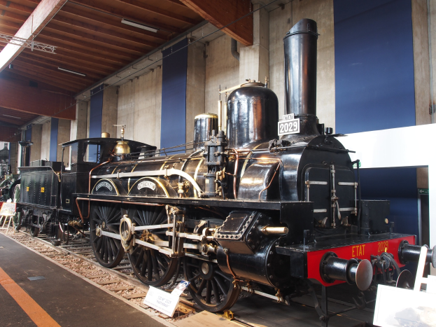 Alte Dampflokomotive in einem Museums Setting mit Eisenbahnschienen, Informationsschildern und Beleuchtungselementen.
