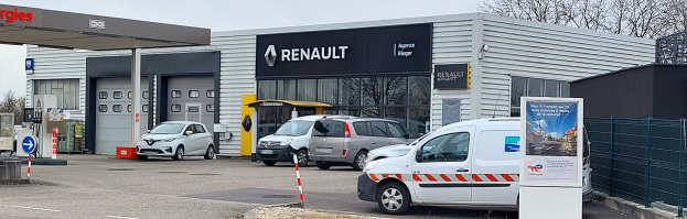 Eine Renault-Vertretung mit parkenden Autos davor, umgeben von einem Metallzaun, mit einem Schild, Pfosten, einer Texttafel, Bäumen und einem bewölkten Himmel.