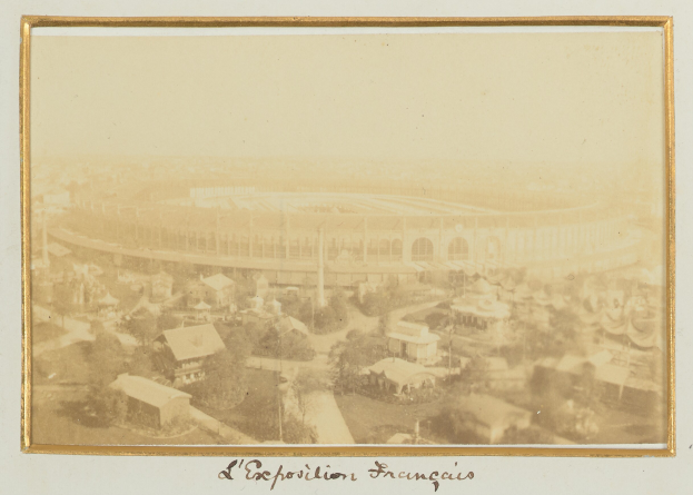 Altes Foto eines Stadions in städtischer Umgebung mit umliegenden Gebäuden, Bäumen und Masten, mit Text unten.