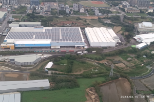 Luftaufnahme eines großen Industriegebiets mit Gebäuden, Bäumen, Gras, Straßen, Fahrzeugen, Masten und einem Wasserzeichen, das die erste Solarstromanlage in Singapur in der rechten unteren Ecke anzeigt.