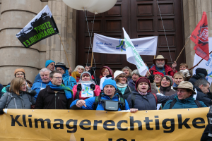 Eine Gruppe von Menschen vor einem Säulengebäude mit einer Tür, die eine Transparente mit Text, Fahnenstangen und Luftballons halten, nimmt an einem Klimastreik in Deutschland teil.
