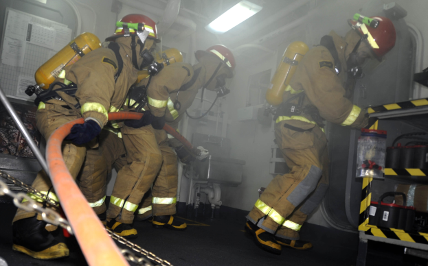 Feuerwehrleute in Schutzausrüstung arbeiten an einem Feuerwehrauto mit Ausrückungsgestellen und Hintergrundinfrastruktur.