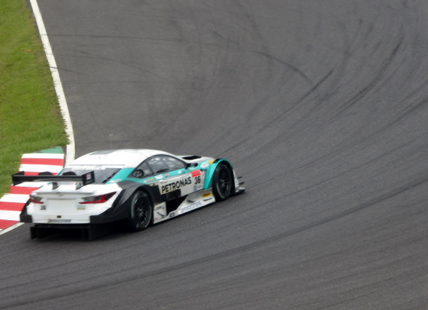 Ein Mercedes-AMG GT3 Rennwagen auf einer Rennstrecke mit Text auf der Karosserie und Gras auf der linken Seite.