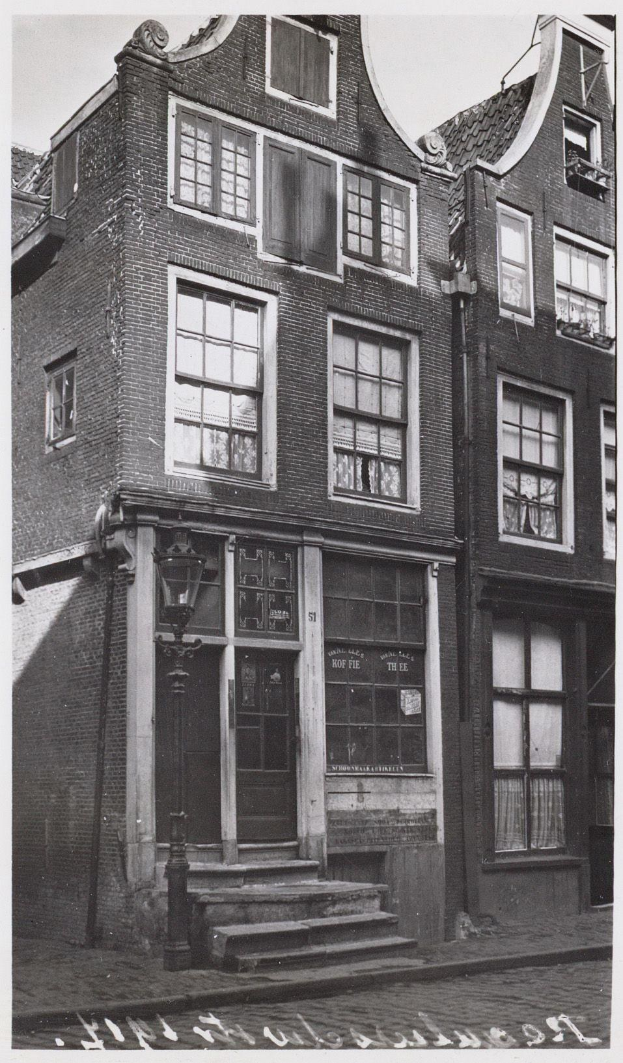 Schwarzes und weißes Foto eines alten Gebäudes in Brügge, Belgien, circa 1900, mit Fenstern, einer Tür, Stufen, einem Laternenpfahl und einem Himmel im Hintergrund.