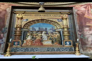 Ein Altar in einer Kirche mit Skulpturen, Kerzen und anderen Gegenständen, vor einer Wand mit einem Bild und einer Pflanze unten.