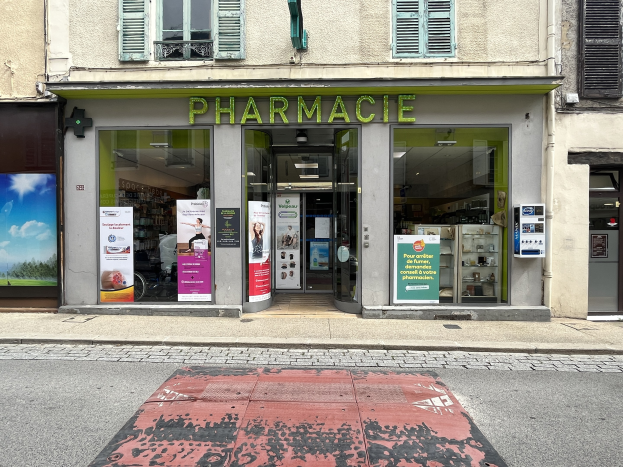 Apotheke mit Glaswänden und -türen, Plakate an den Innenwänden, an einer Straßenecke gelegen.