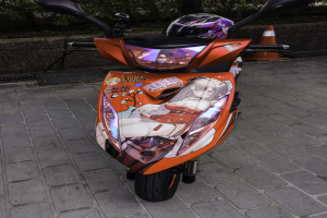 Ein oranges Elektro-Scooter-Fahrzeug, das auf einer Straße mit einem Helm daneben geparkt ist, neben einem Verkehrskegel, einer Wand und Bäumen im Hintergrund.